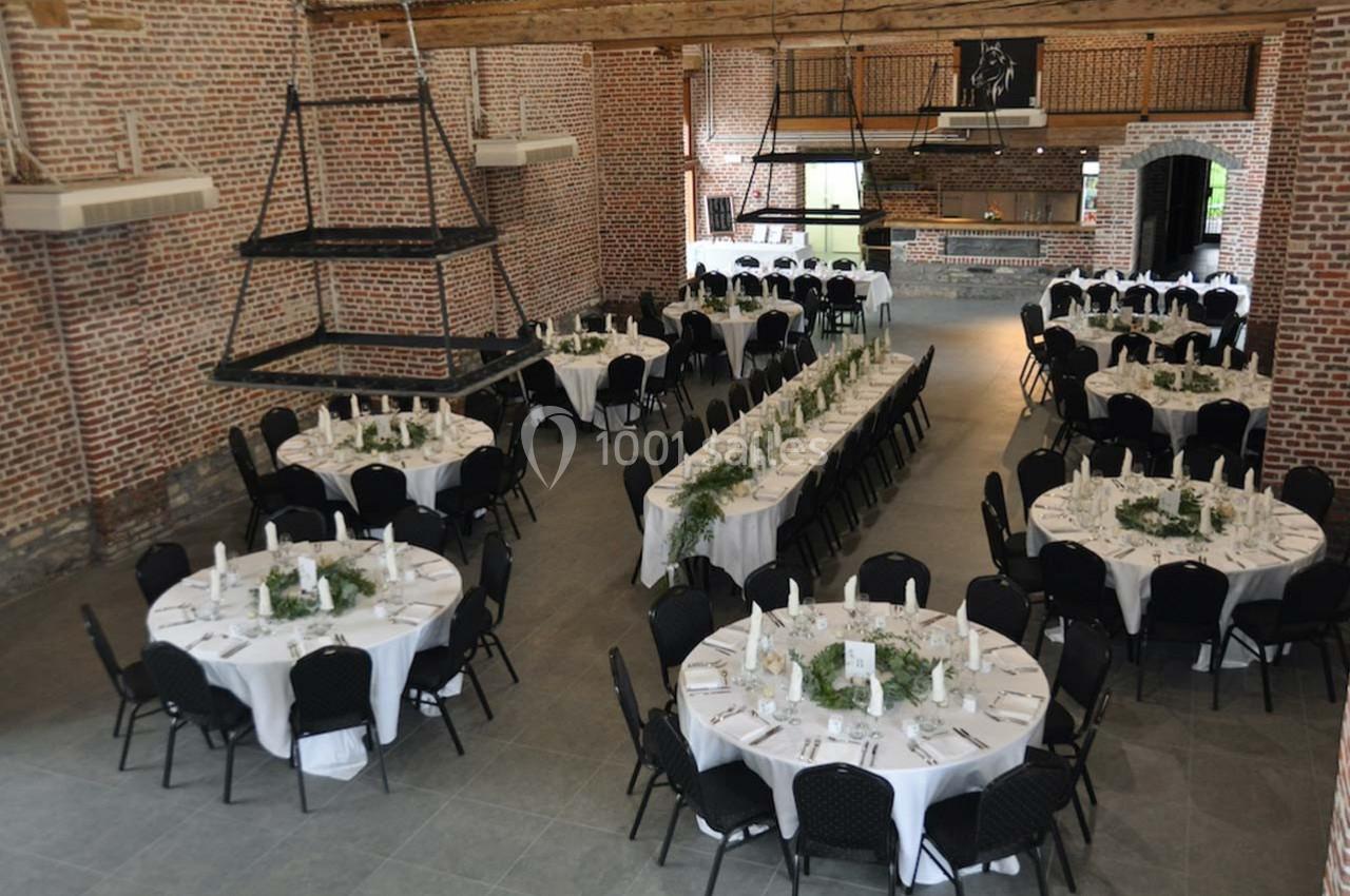 Salle de réception en briques avec tables rondes et rectangulaires dressées pour un événement.