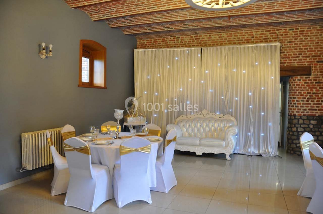 Salle décorée avec des murs en briques, un canapé blanc capitonné, des chaises habillées et une table dressée.