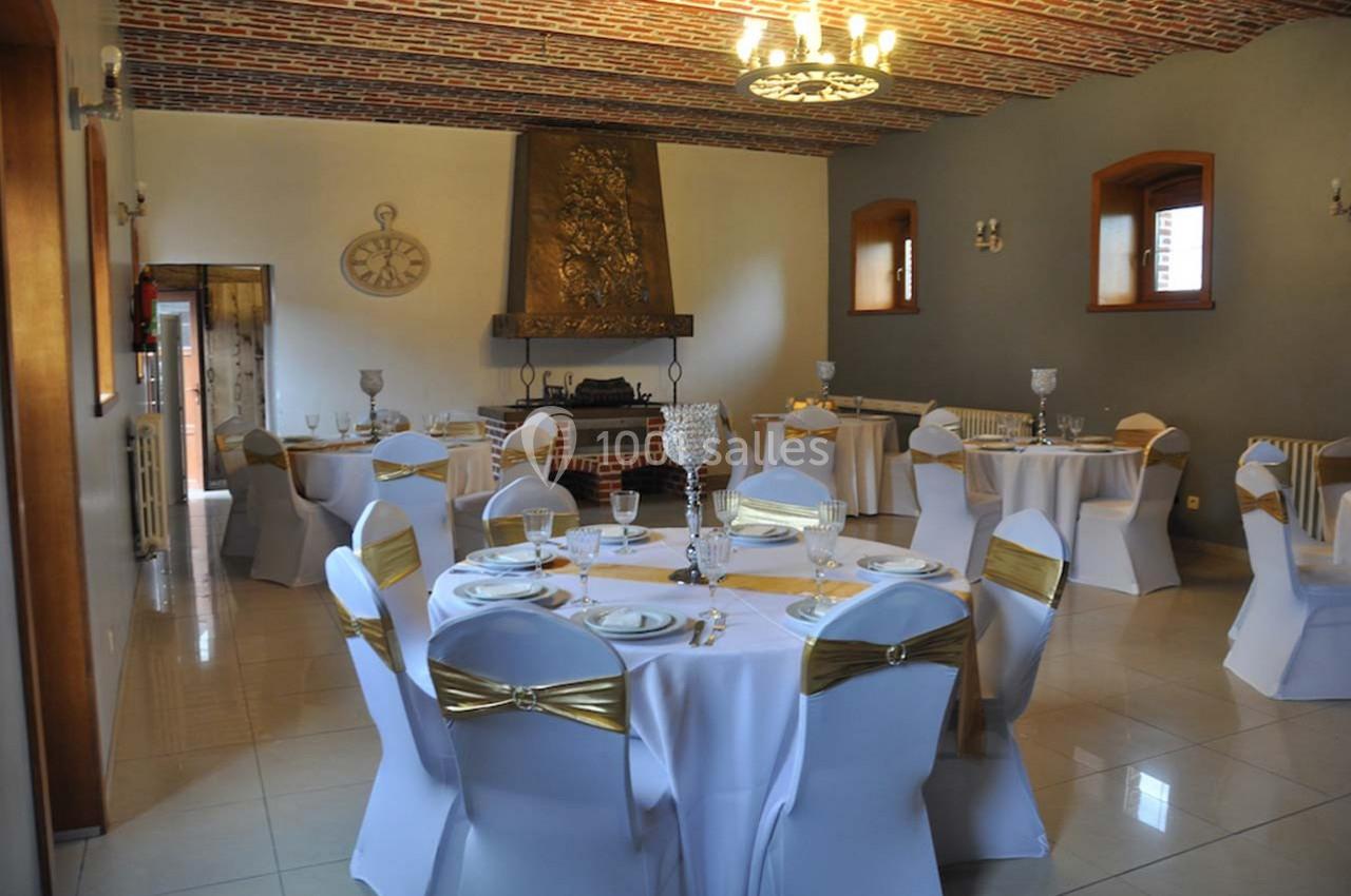 Salle de réception élégante avec tables rondes dressées, nappes blanches et chaises décorées de nœuds dorés.