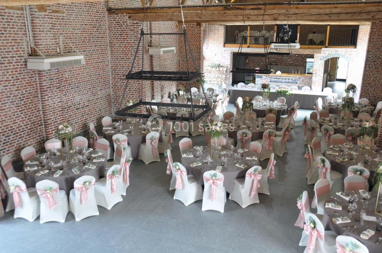 Salle de réception décorée avec des tables rondes, nappes blanches et chaises ornées de rubans roses.