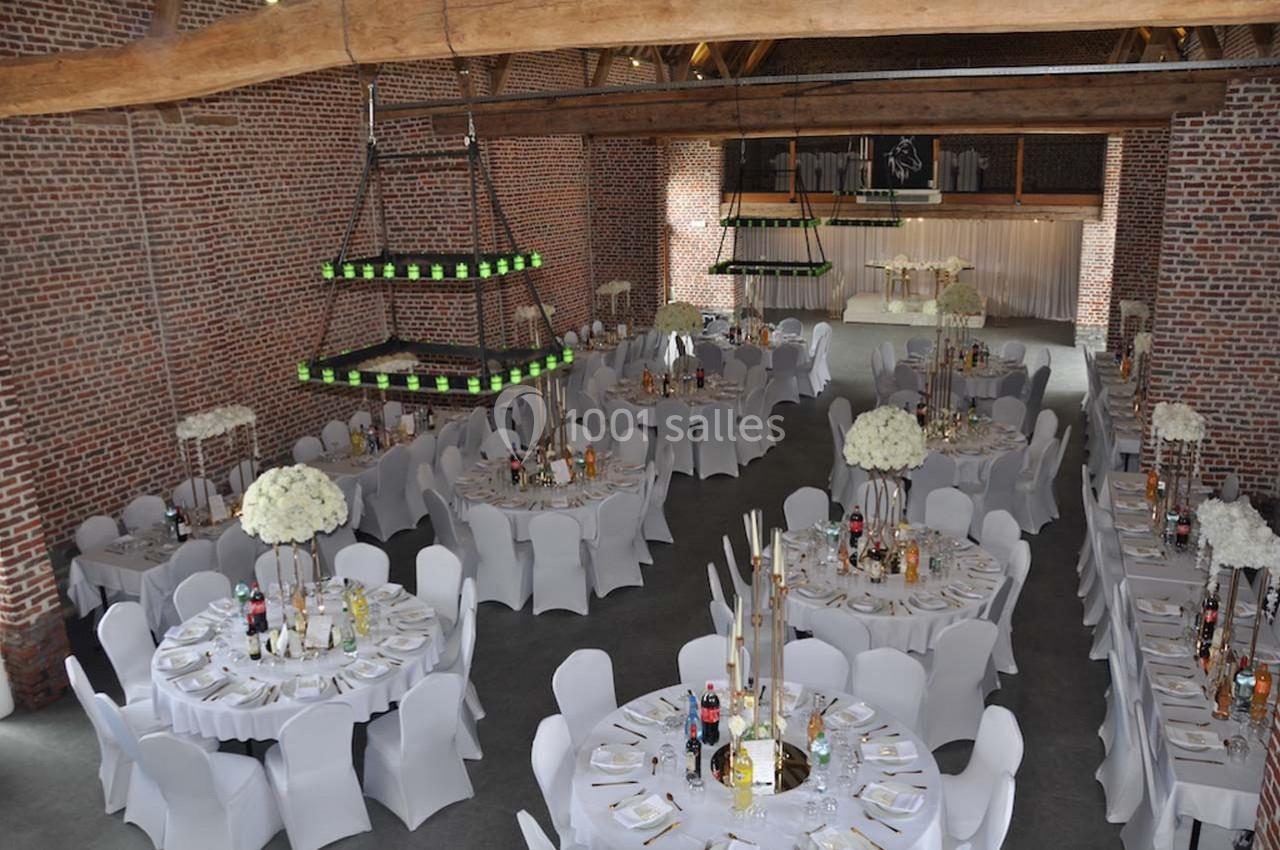 Salle de réception avec tables rondes décorées, nappes blanches, chaises assorties et éclairage suspendu.
