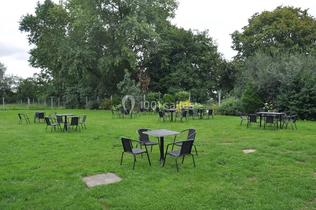 Tables et chaises noires disposées sur une pelouse verte entourée d'arbres et de buissons.