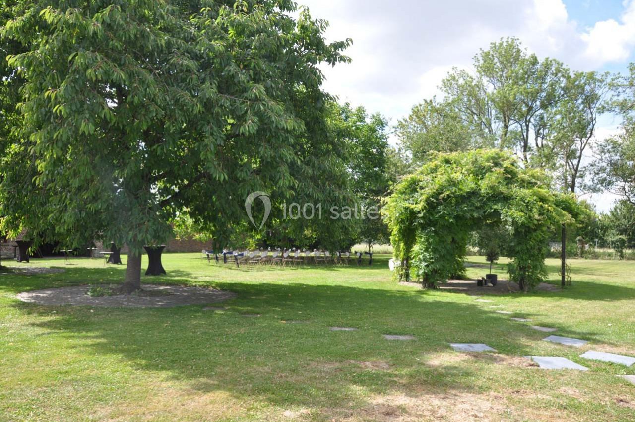 Jardin verdoyant avec un grand arbre, une tonnelle couverte de végétation et des chaises disposées en arrière-plan.