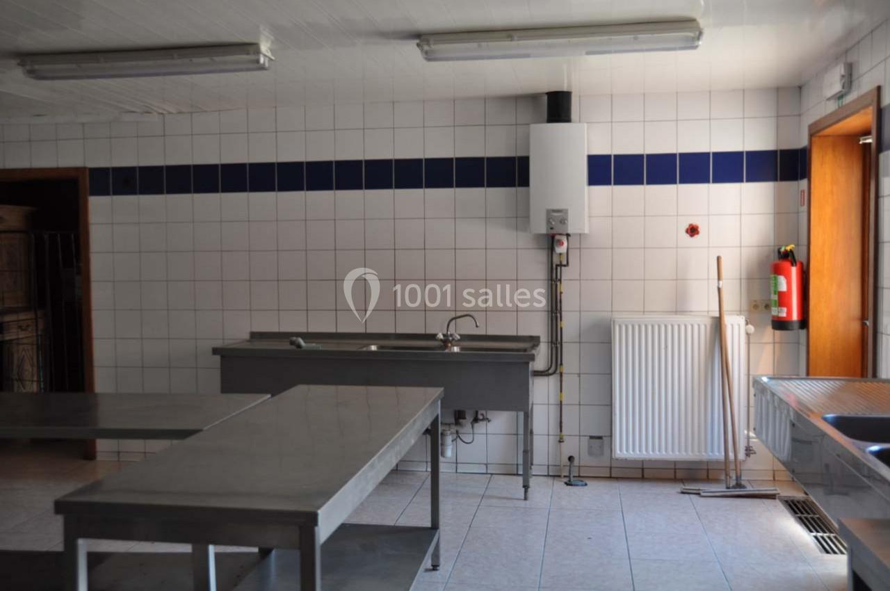 Cuisine professionnelle vide avec murs carrelés blancs, plans de travail en inox, évier, chauffe-eau et matériel de…