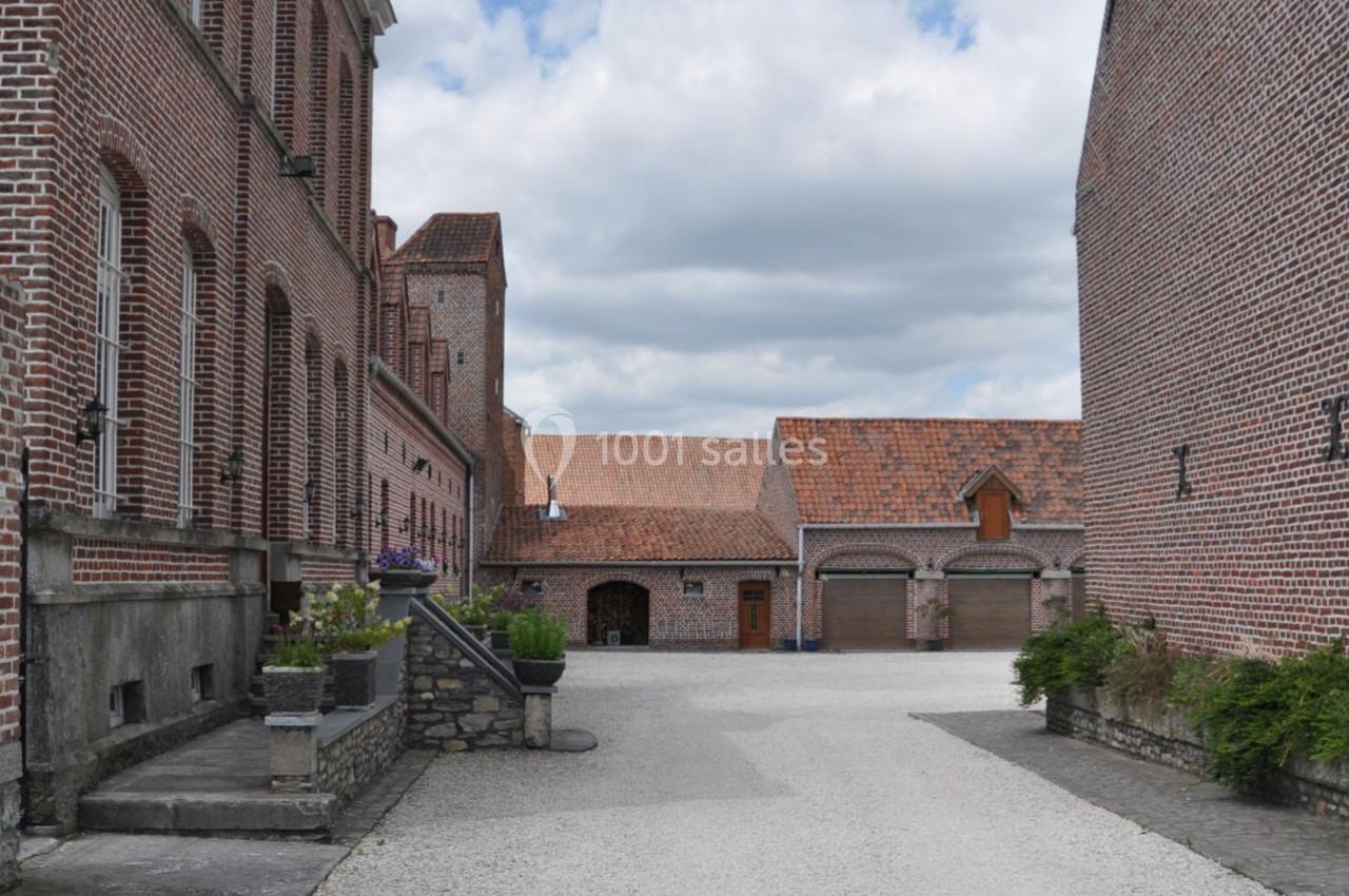 Cour pavée entourée de bâtiments en briques rouges avec toits en tuiles, sous un ciel partiellement nuageux.