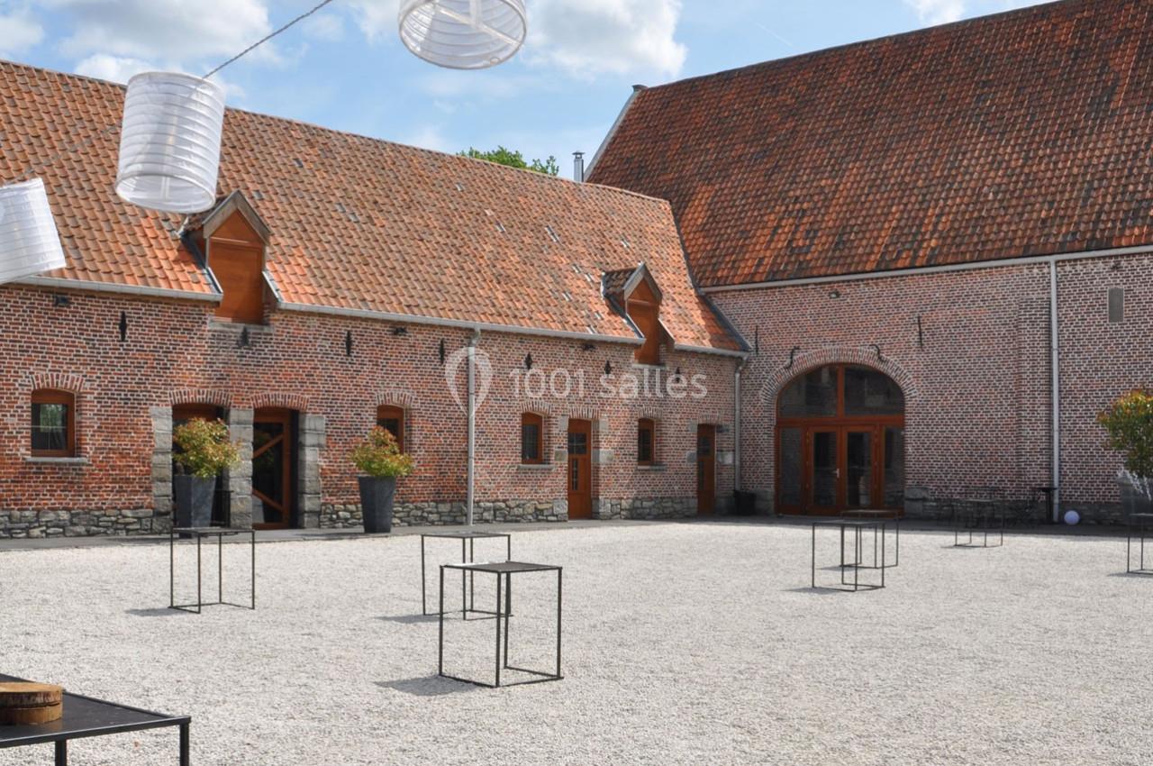 Cour pavée avec des bâtiments en briques rouges, des tables métalliques et des lanternes suspendues sous un ciel…
