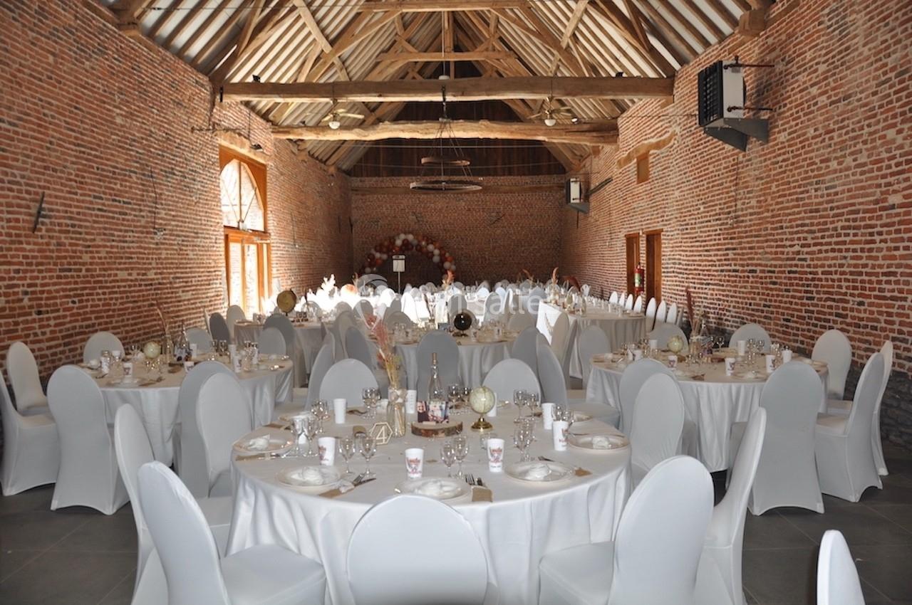 Salle de réception en briques avec tables rondes dressées, nappes blanches et décoration de mariage.