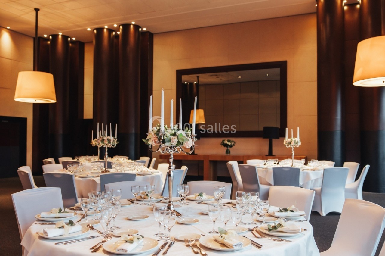 Salle élégante avec tables rondes dressées, nappes blanches, chandeliers et décorations florales.