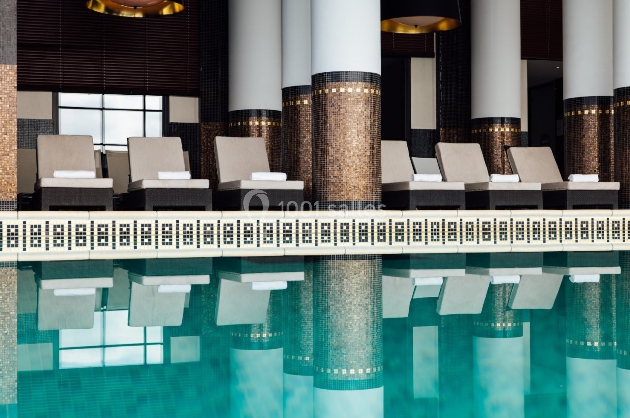 Chaises longues alignées près d'une piscine intérieure, entourée de colonnes et de décorations murales élégantes.