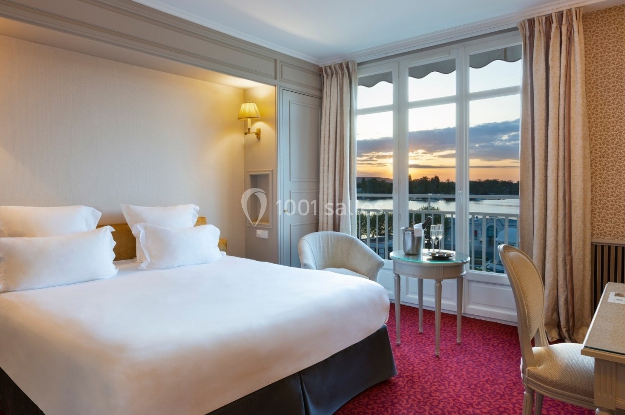 Chambre lumineuse avec lit double, table, chaises et grande fenêtre offrant une vue sur un coucher de soleil.