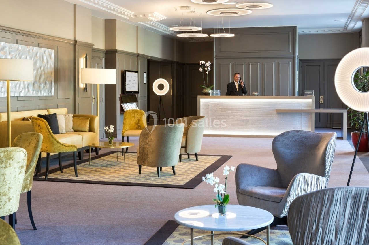 Salon d'accueil élégant avec fauteuils, tables basses, éclairage moderne et réceptionniste au comptoir lumineux.