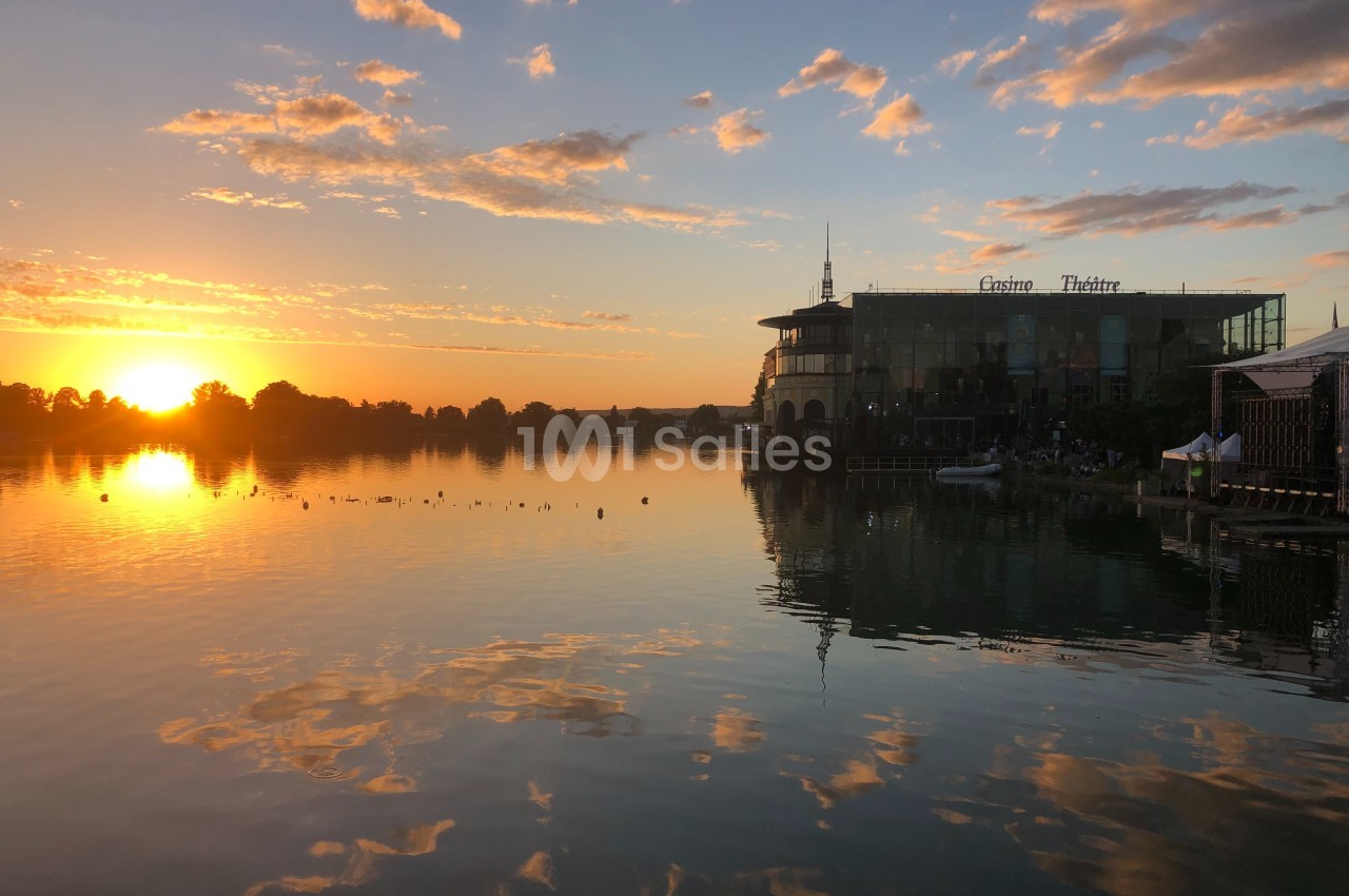 Coucher de soleil sur un lac avec des reflets dorés, un bâtiment et des nuages légers à l'horizon.