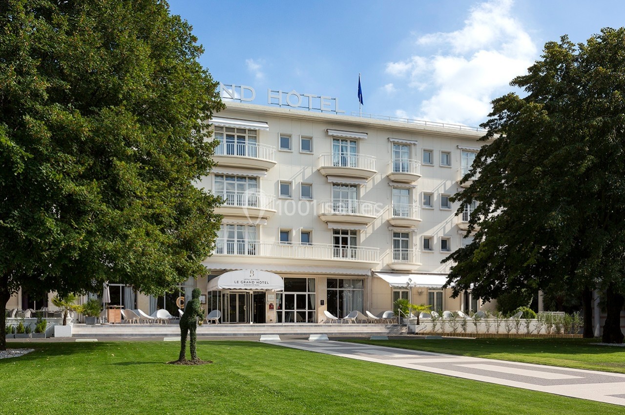 Façade d'un hôtel blanc entouré d'arbres, avec une pelouse bien entretenue au premier plan.