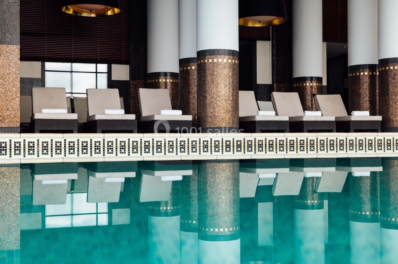 Chaises longues alignées près d'une piscine intérieure avec colonnes et mosaïques décoratives.