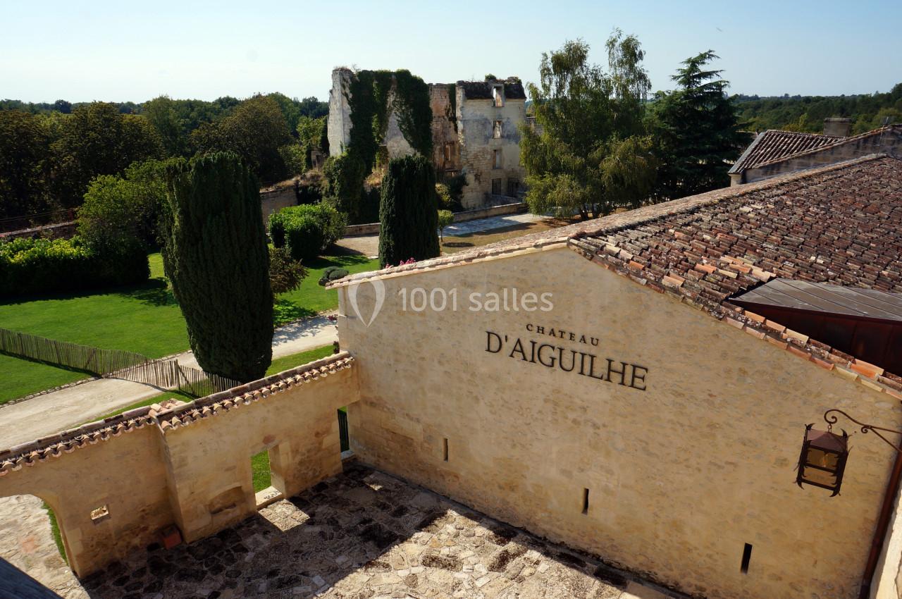Vue d'un château en pierre avec des ruines à l'arrière-plan, entouré de verdure et d'arbres.