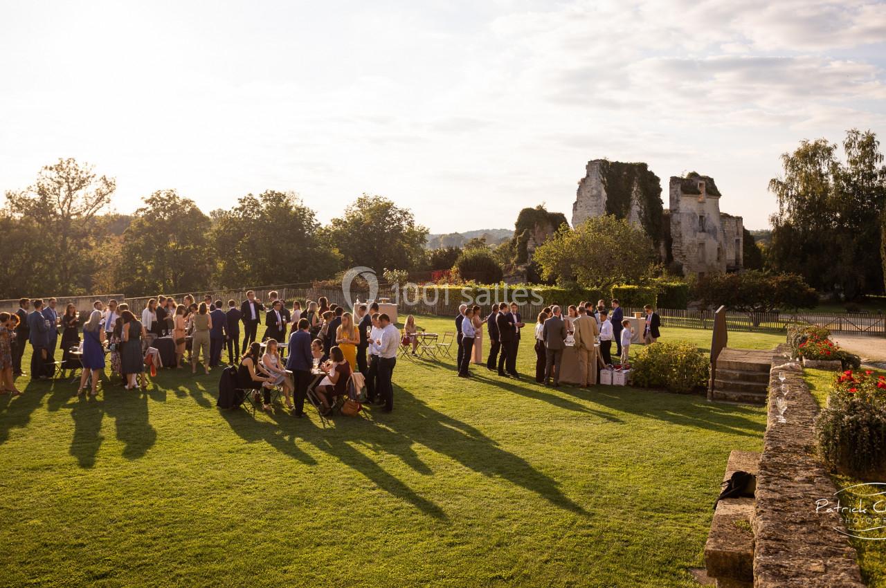 Groupe de personnes rassemblées sur une pelouse au coucher du soleil, avec des ruines historiques en arrière-plan.