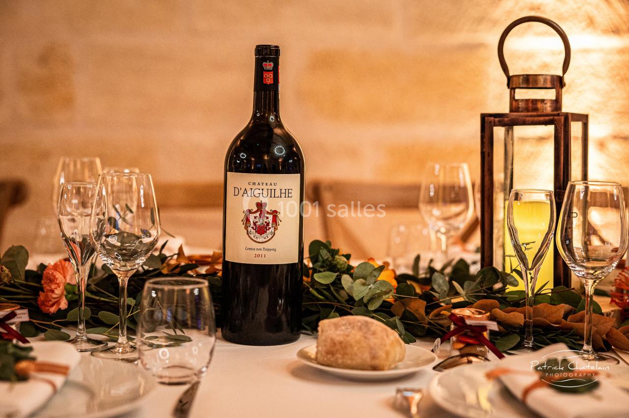 Bouteille de vin rouge sur une table décorée avec des verres, des fleurs et une lanterne en arrière-plan.