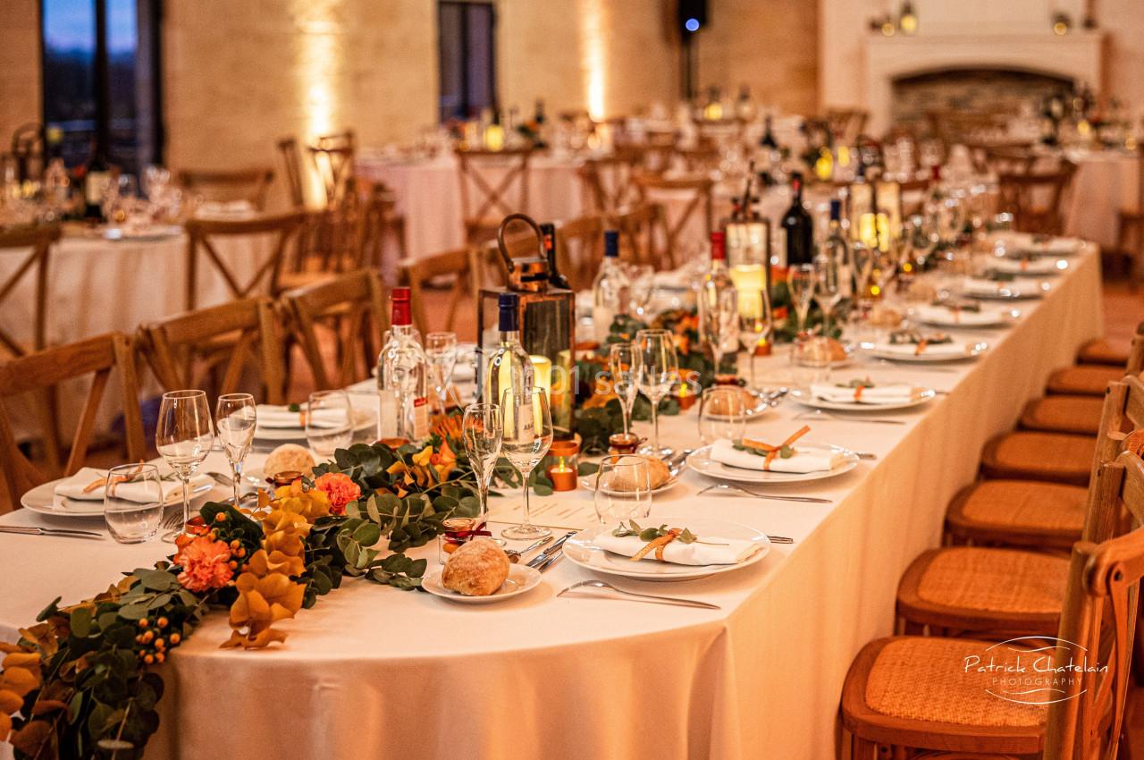 Table de réception élégamment dressée avec vaisselle, bougies, bouteilles et décoration florale dans une salle chaleureuse.