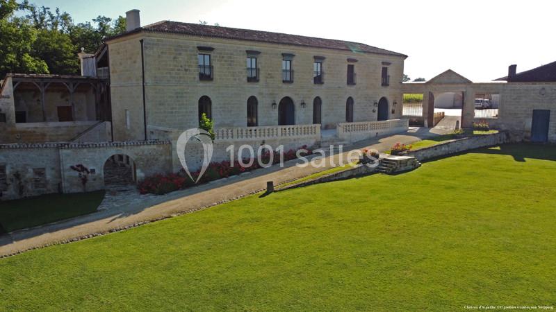 Bâtiment en pierre avec balustrade, entouré de pelouse et de parterres fleuris, sous un ciel dégagé.