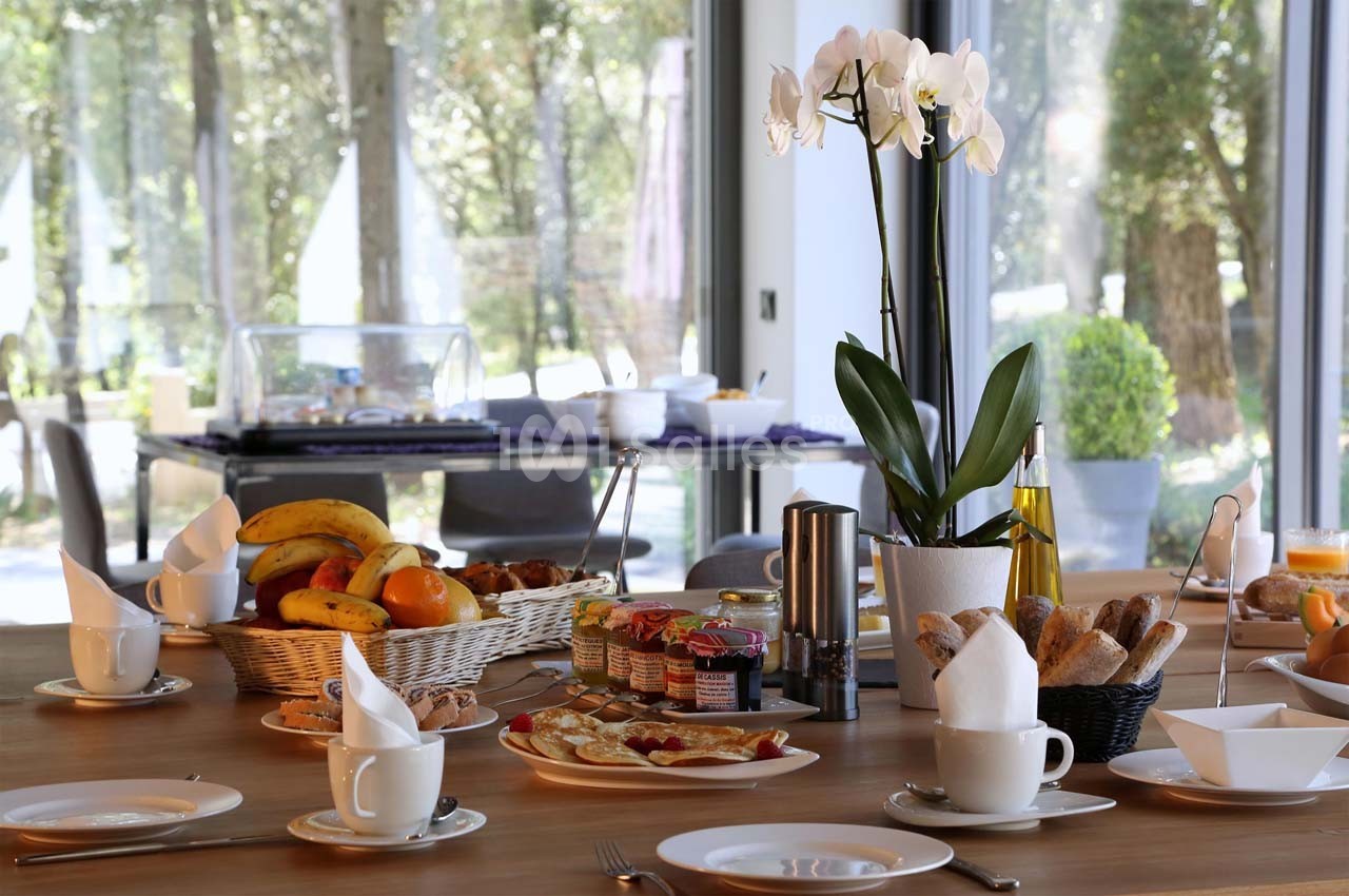 Table dressée pour un petit-déjeuner avec fruits, viennoiseries, confitures, et une orchidée en décoration.