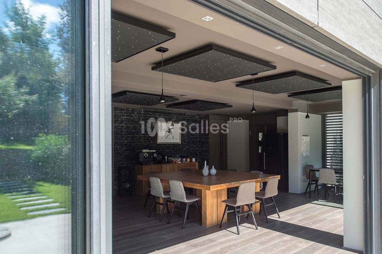 Vue d'une salle à manger moderne avec table en bois, chaises assorties et plafond décoré de panneaux lumineux.