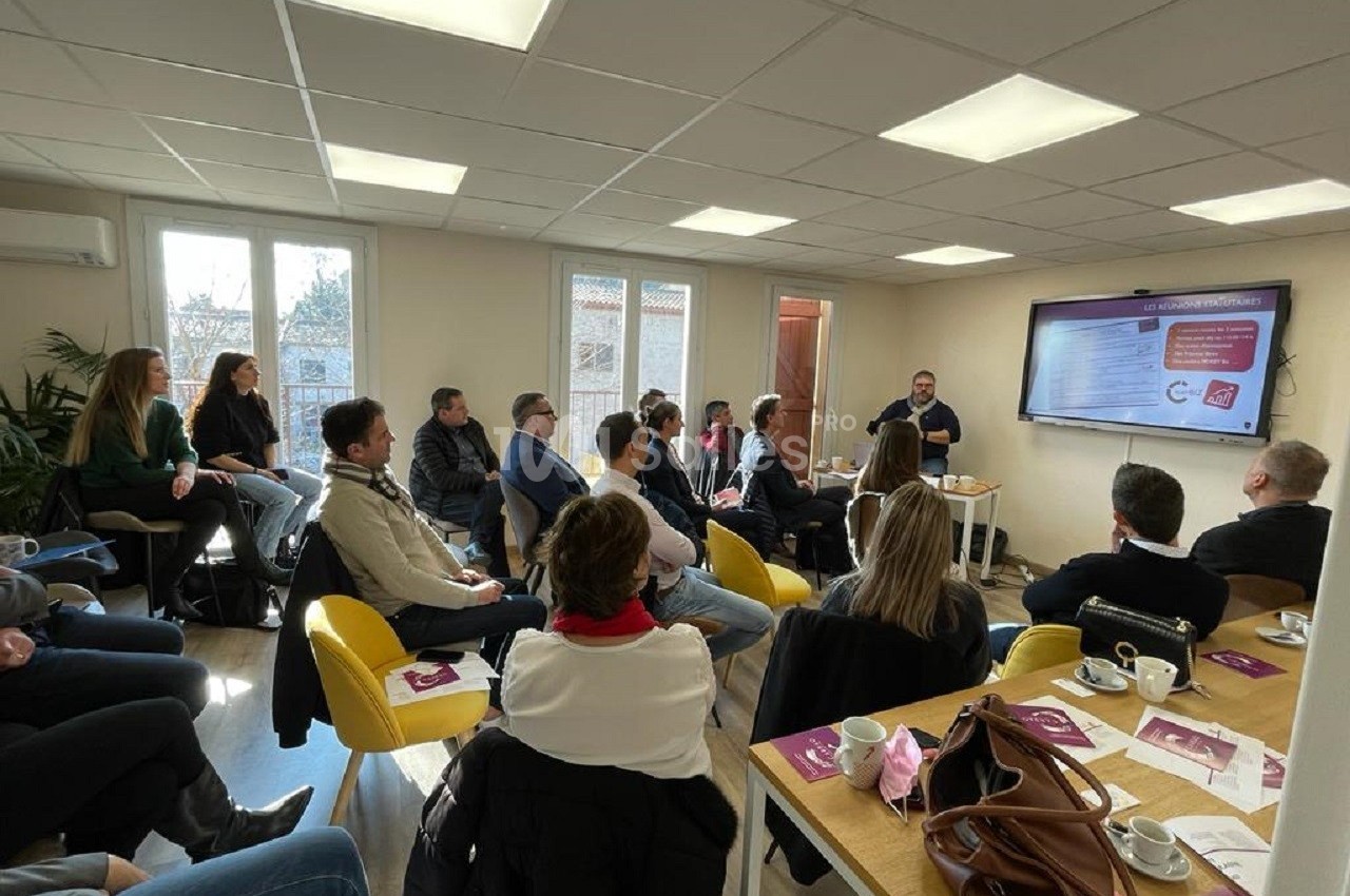 Un groupe de personnes assises dans une salle de réunion, écoutant une présentation affichée sur un écran.