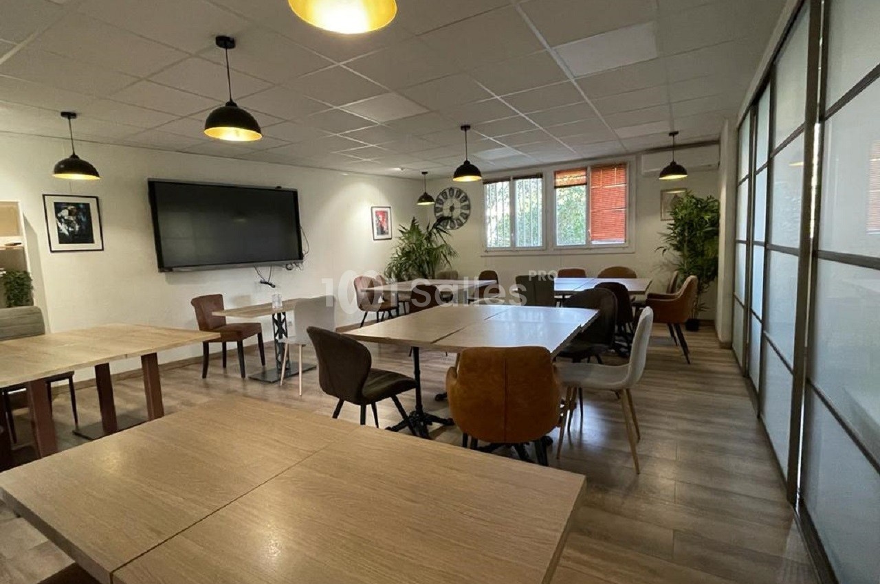 Salle de réunion lumineuse avec tables en bois, chaises variées, écran mural et plantes décoratives.