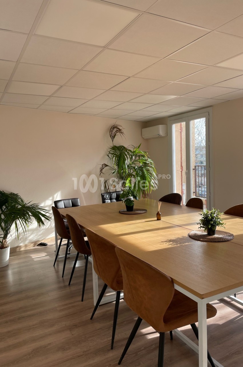 Salle de réunion lumineuse avec une grande table en bois, des chaises en cuir et des plantes décoratives.