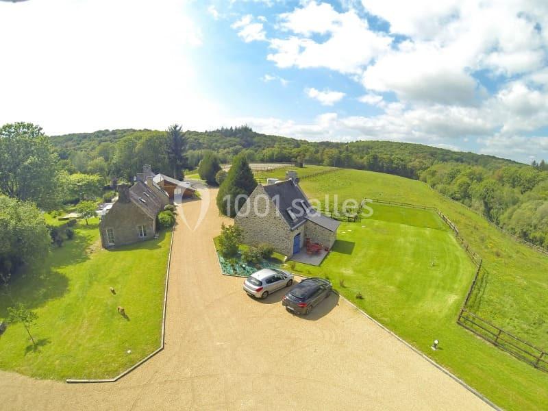 Vue aérienne de deux maisons en pierre entourées de pelouses, d'arbres et d'une allée gravillonnée en campagne.