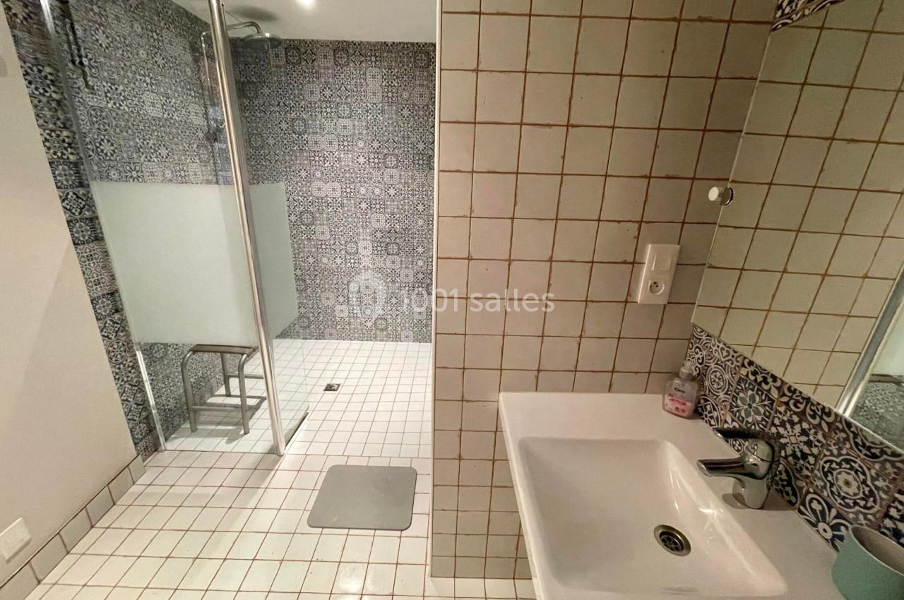 Salle de bain avec douche à l'italienne, carrelage à motifs et mur en carreaux blancs, lavabo avec miroir.