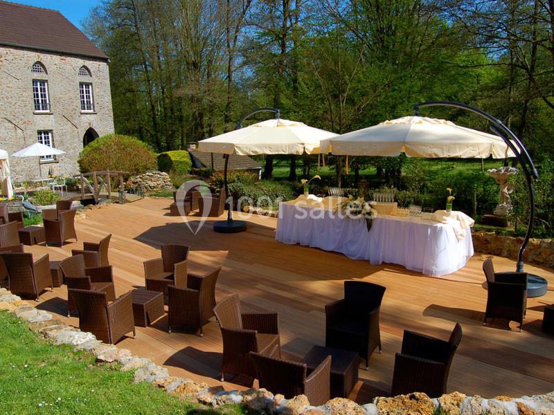 Terrasse en bois aménagée avec des fauteuils en rotin, des parasols et une table dressée dans un cadre verdoyant.