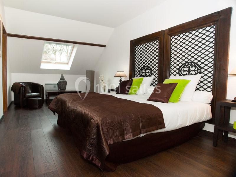 Chambre avec deux lits simples, tête de lit en bois sculpté, parquet sombre et fenêtre de toit apportant de la lumière.