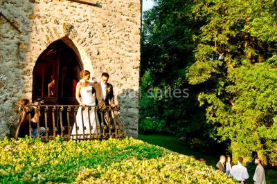 Un couple en tenue de mariage se tient sur un balcon en pierre devant une fenêtre illuminée.
