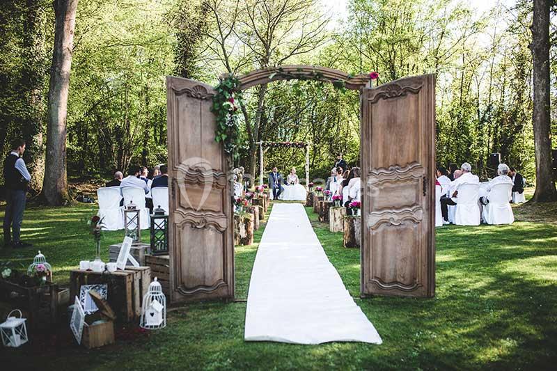 Cérémonie de mariage en plein air avec allée centrale bordée de chaises et arche décorée de fleurs.
