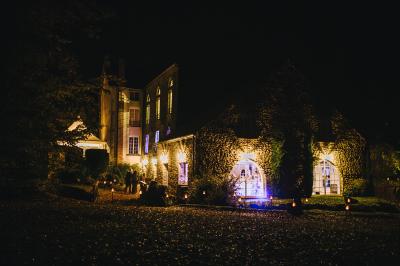 Un couple en tenue de mariage se tient sur un balcon en pierre devant une fenêtre illuminée.