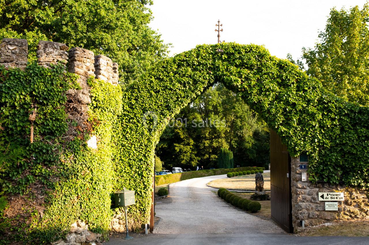 Portail en pierre recouvert de lierre, ouvert sur une allée bordée de verdure et menant à un espace arboré.