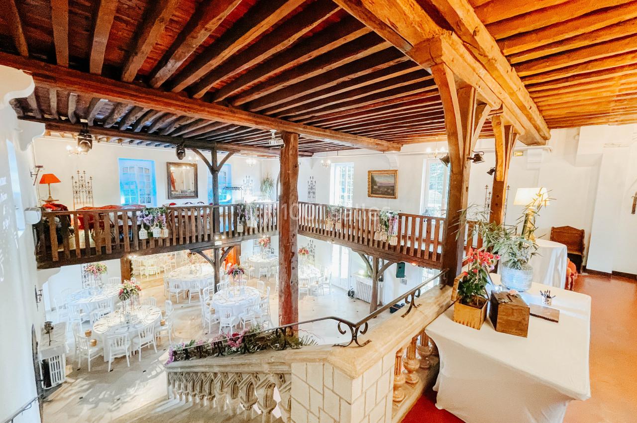 Salle lumineuse avec mezzanine en bois, tables dressées pour un événement et décoration florale élégante.
