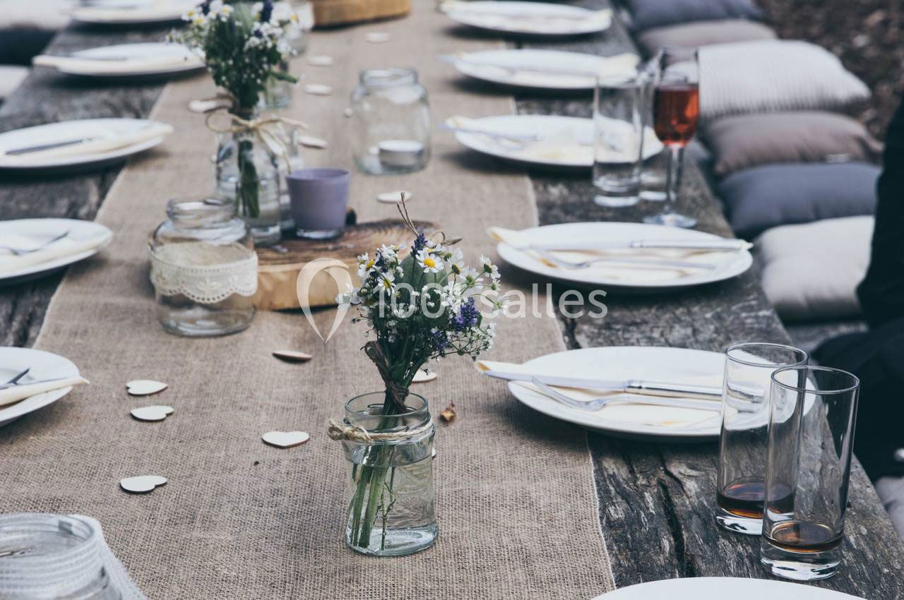 Table en bois rustique décorée de fleurs sauvages, vaisselle blanche et verres, prête pour un repas en extérieur.