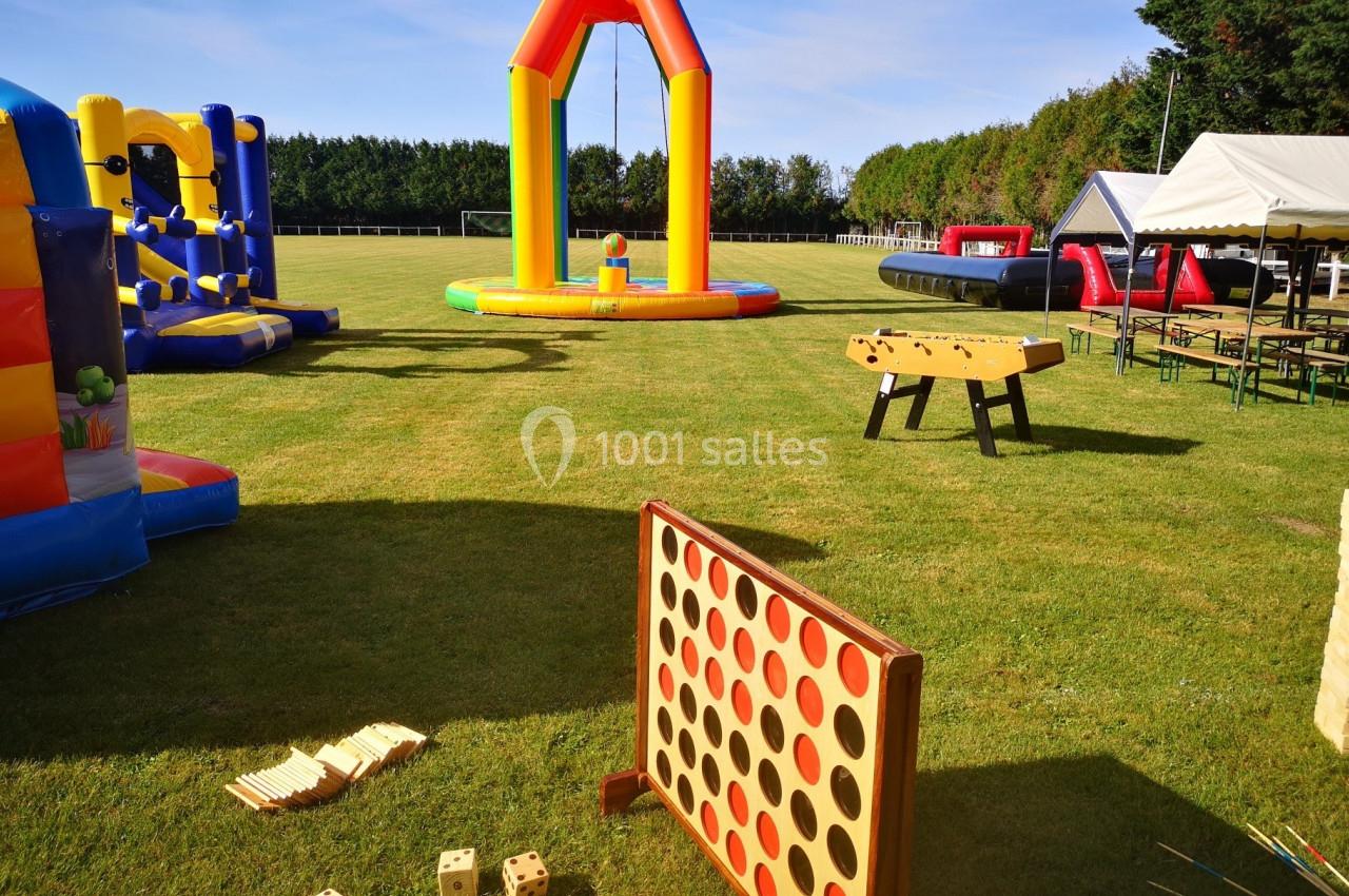Jeux en plein air sur une pelouse, incluant structures gonflables, puissance 4 géant et baby-foot.