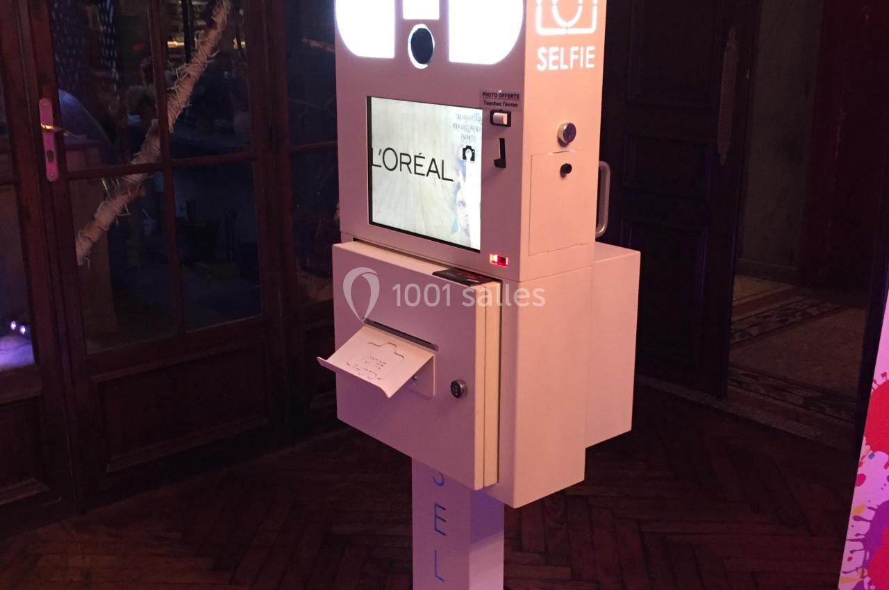 Borne photo interactive avec écran, imprimante et éclairage, installée dans un espace intérieur sombre.