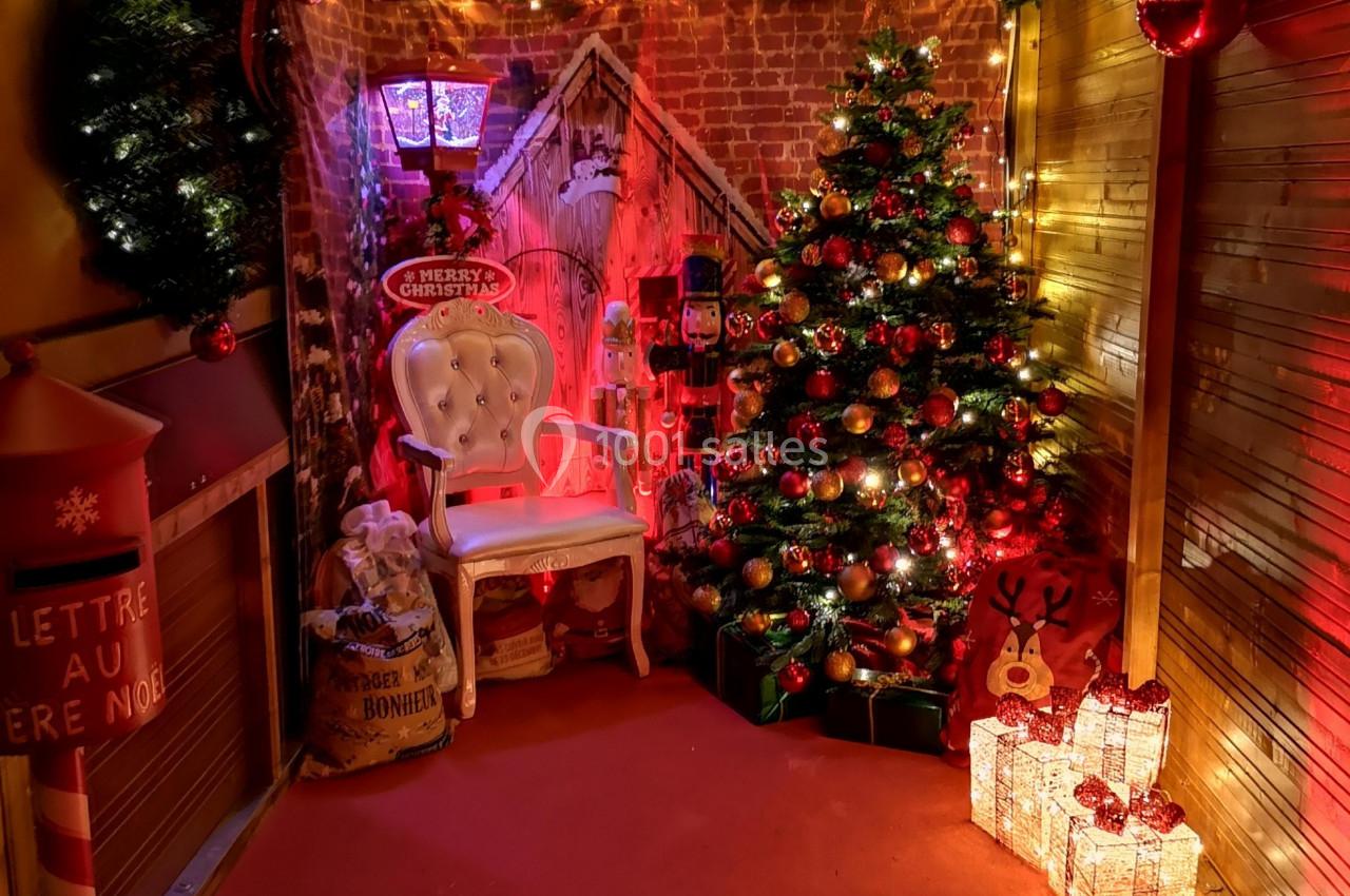 Décoration de Noël avec sapin illuminé, guirlandes, cadeaux, fauteuil blanc et boîte aux lettres festive.
