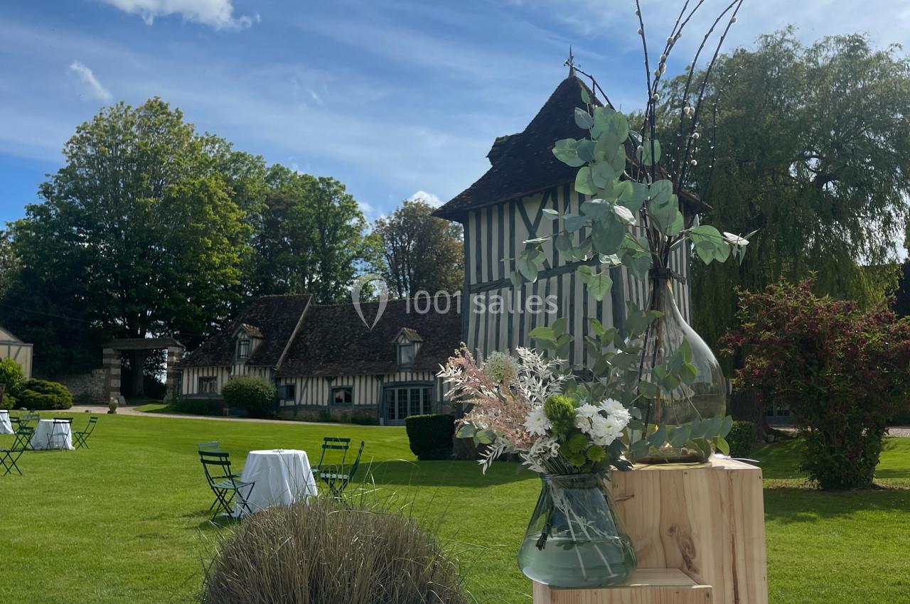 Table décorée avec des fleurs et des éléments en bois, installée dans un jardin devant une maison à colombages.