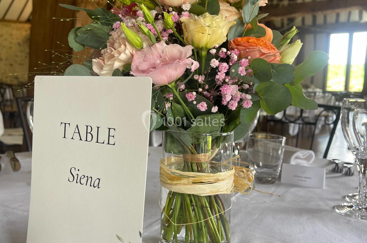 Centre de table avec bouquet de fleurs pastel dans un vase, carte indiquant ’Table Siena’ sur une table dressée.