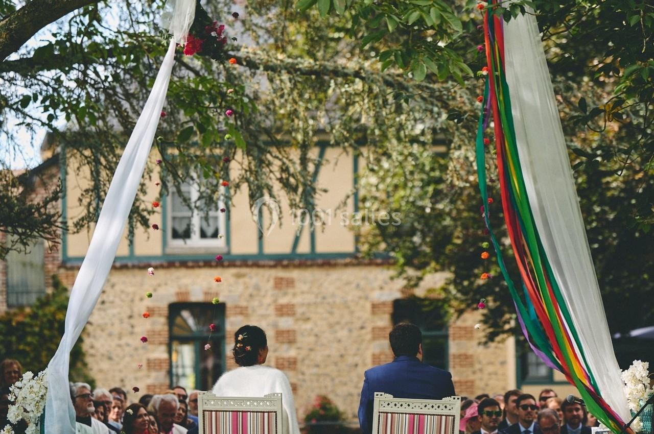 Un couple assis sous un arbre décoré, face à des invités lors d'une cérémonie en plein air.