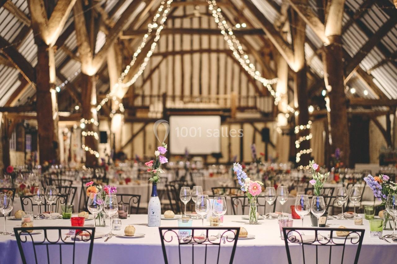 Salle de réception décorée avec des guirlandes lumineuses, tables dressées avec fleurs et verres.