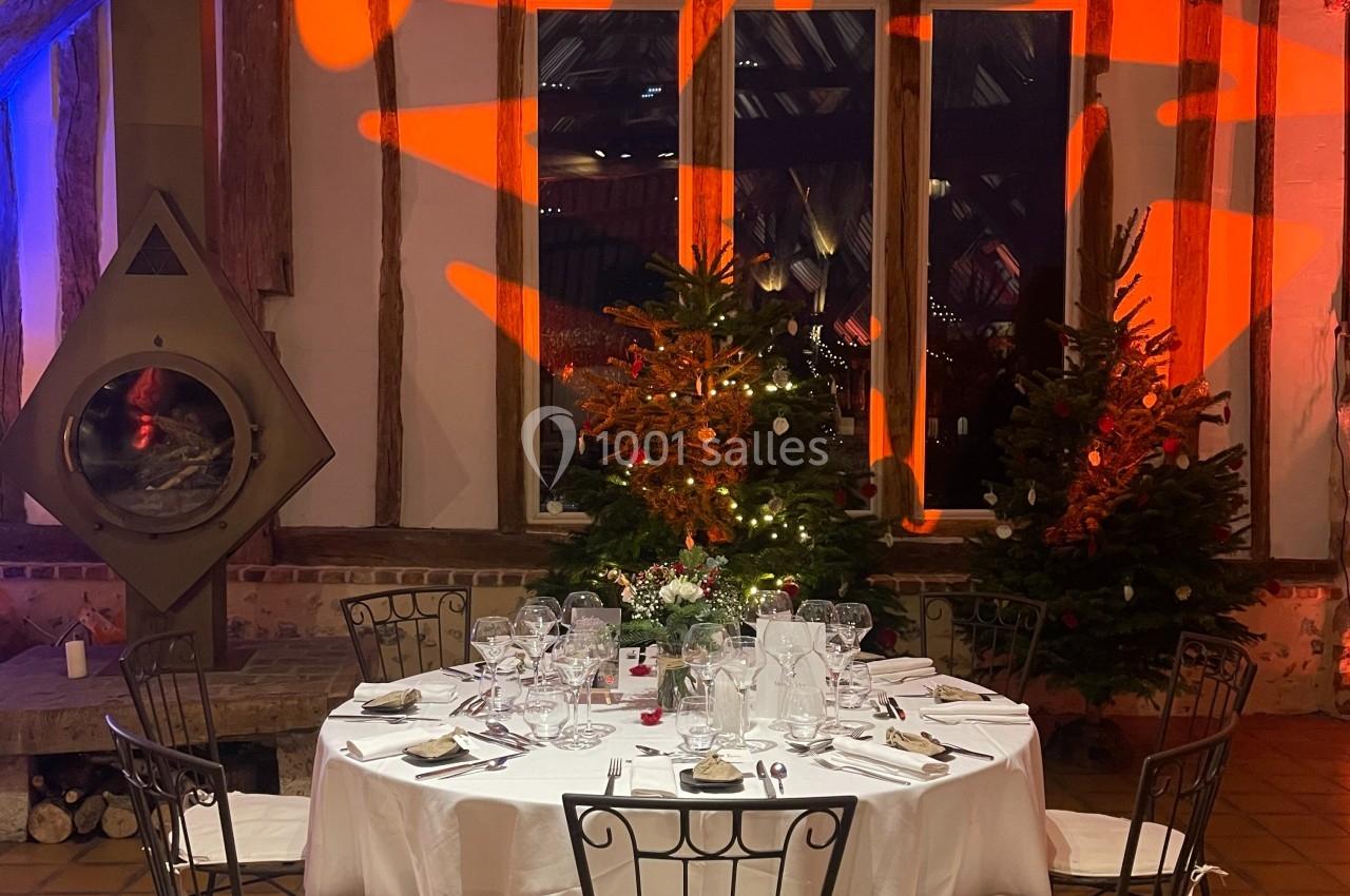 Table ronde dressée avec vaisselle élégante, entourée de chaises en métal, dans une salle rustique décorée de lumières et…