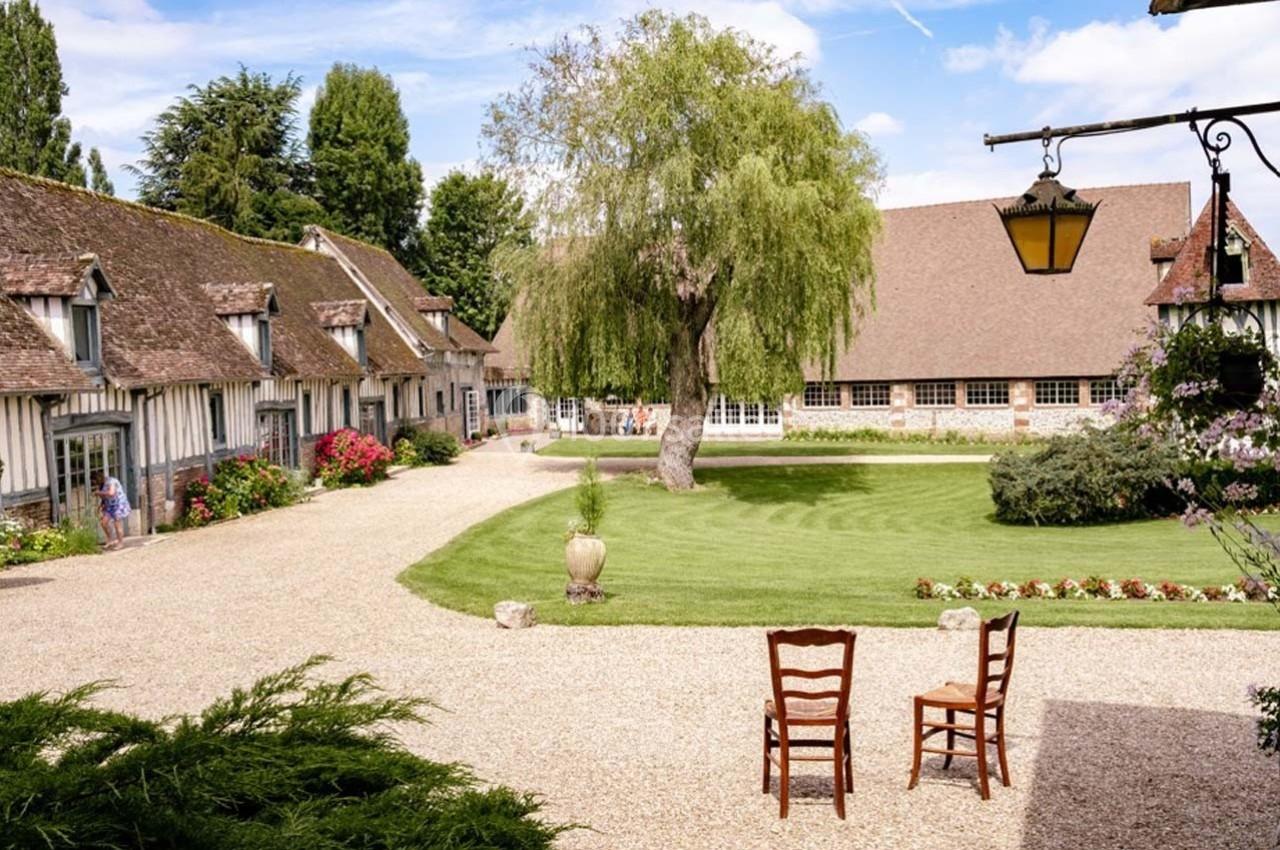 Cour intérieure d'une propriété avec pelouse, allée gravillonnée, bâtiments à colombages et un arbre central.