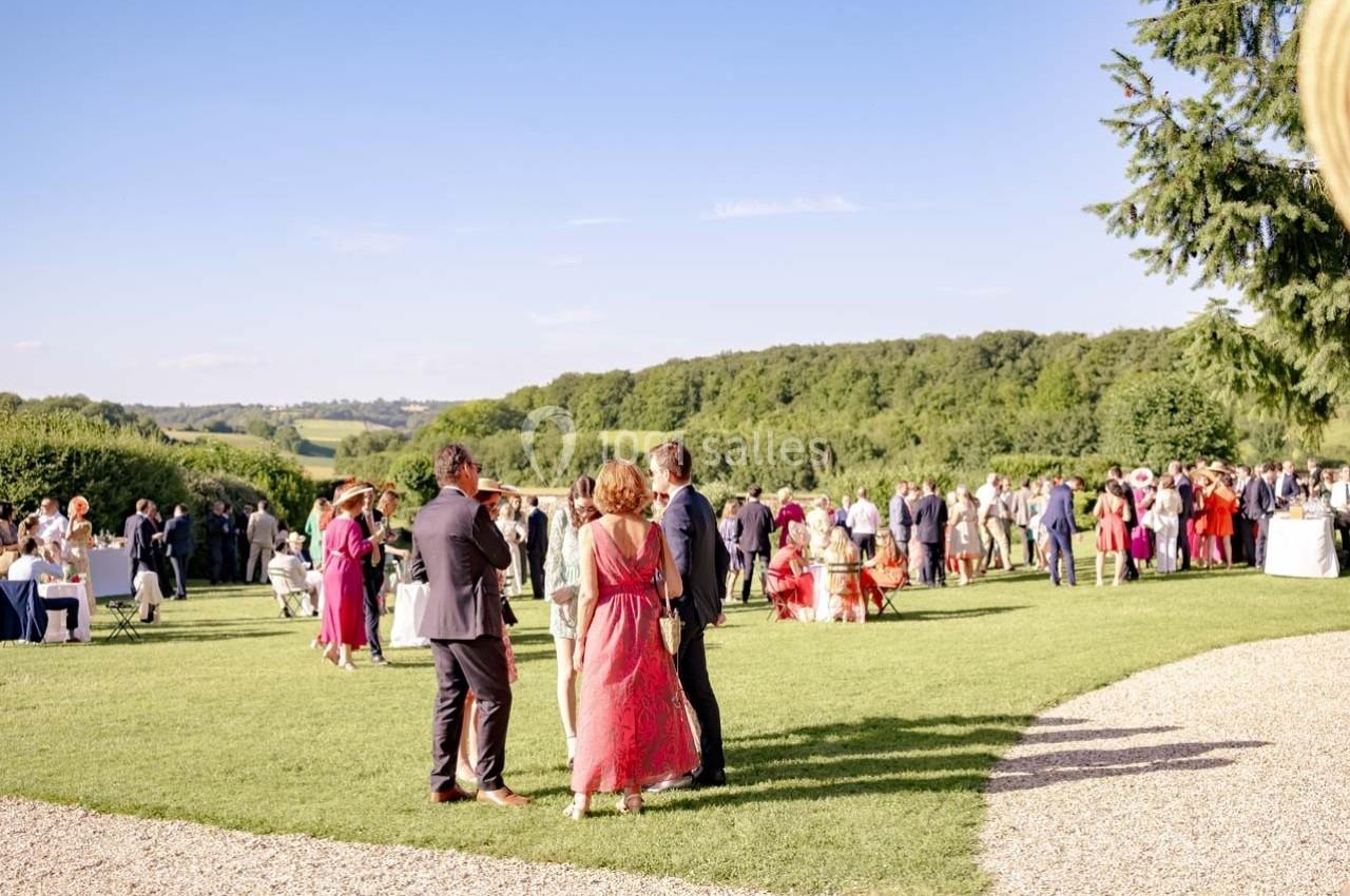 Groupe de personnes élégamment vêtues discutant dans un jardin verdoyant sous un ciel dégagé.