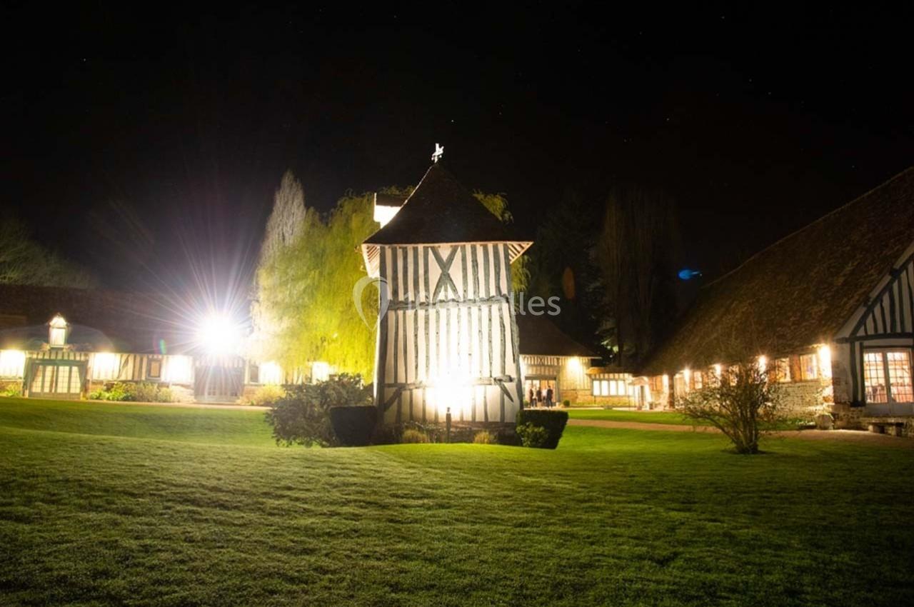 Bâtiment à colombages éclairé la nuit, entouré de pelouses et d'autres structures similaires.