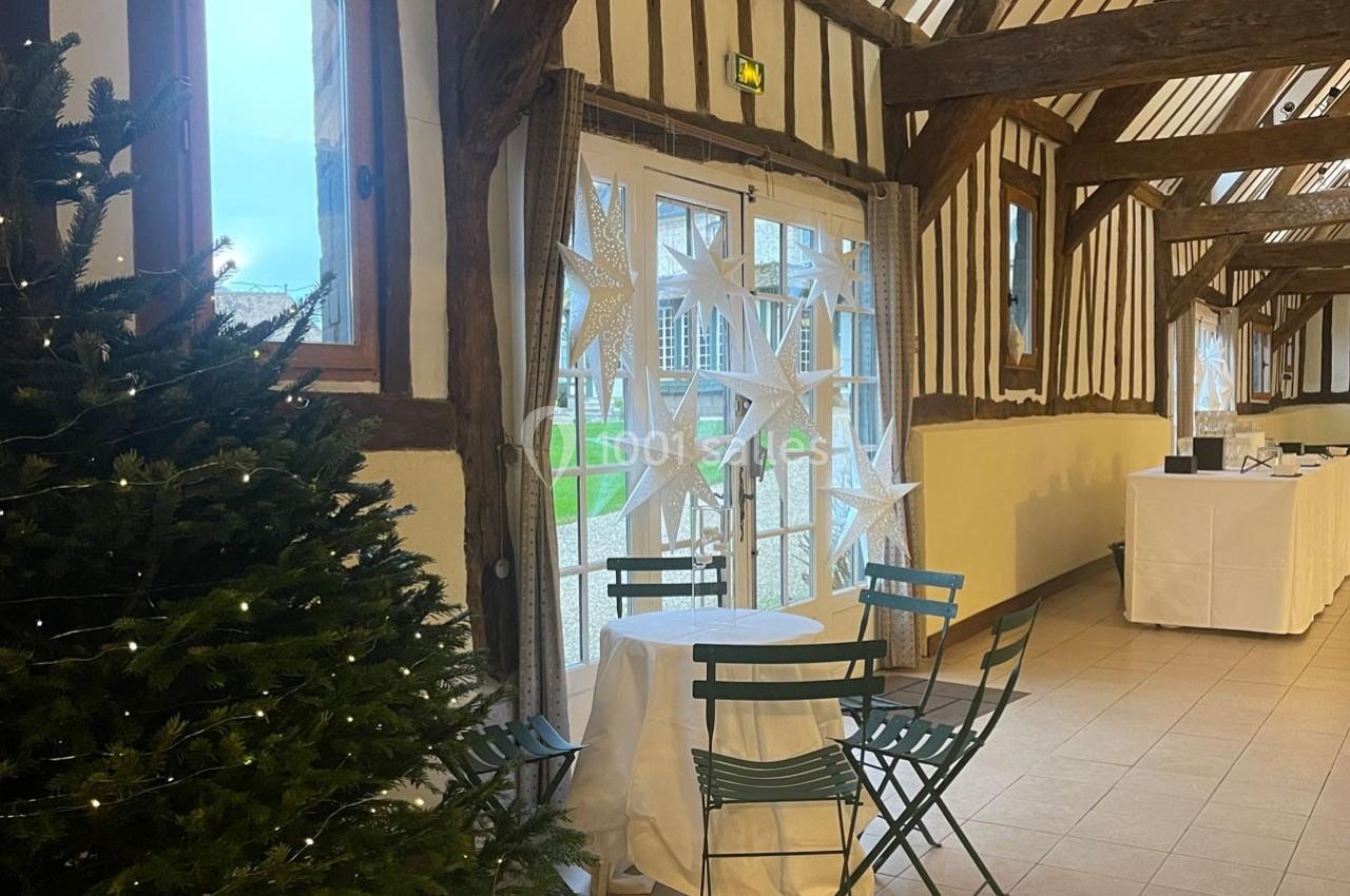 Salle lumineuse avec poutres apparentes, table et chaises près d'un sapin décoré et d'une porte vitrée donnant sur l…